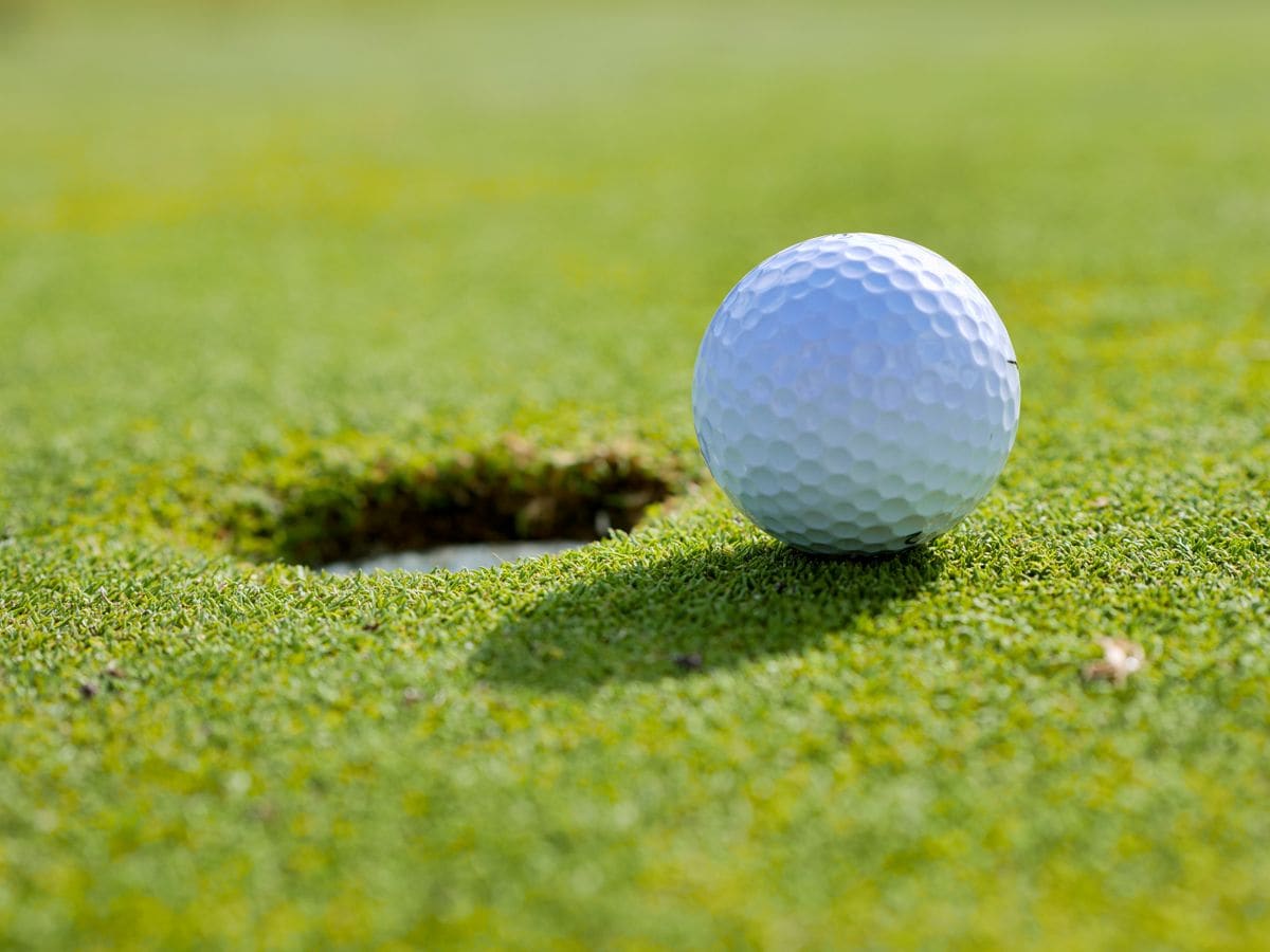 A golf ball at the edge of the hole on a sunlit green